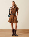 Woman wearing the Ariat Cody Dress with a silver concho belt and dark brown cowboy boots, holding a denim jacket over her shoulder