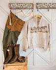 Wrangler x Lainey Wilson brown chap jeans styled with an Ariat horse print sweatshirt