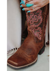 Close-up of Ariat Round Up StretchFit cowboy boot shaft showing pink and red floral embroidery on brown leather, worn by a model with turquoise nail polish and rings