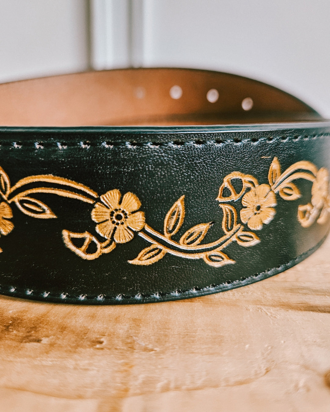 Detail of hand-painted floral tooling on a black leather belt with Western buckle