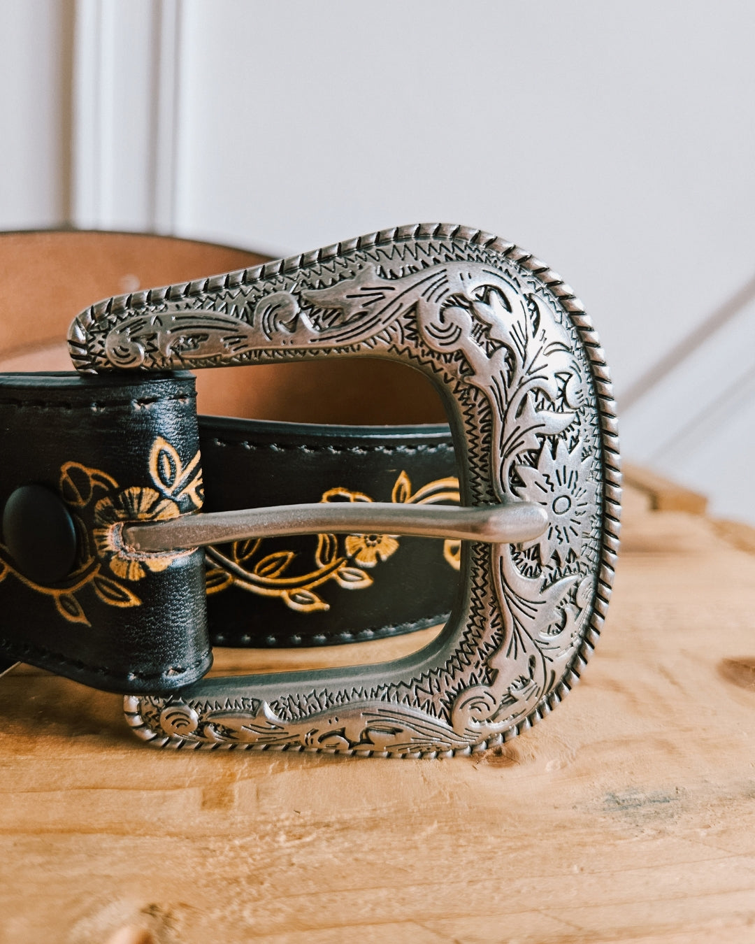 Close-up of the engraved silver Western buckle on a black leather belt