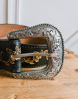 Close-up of the engraved silver Western buckle on a black leather belt
