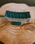 Silver Engraved Western Hair Claw Clip standing upright, showing the teal claw teeth and engraved silver edge, on a rustic wood slice