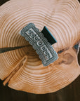 Silver Engraved Western Hair Claw Clip with floral engraving and scalloped edge, displayed on a rustic wood slice