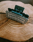 Silver Engraved Western Hair Claw Clip shown open, revealing the teal spring hinge, resting on a rustic wood slice