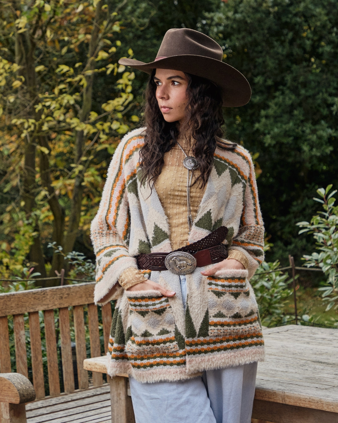 Woman wearing a patterned cardigan and cowboy hat outdoors