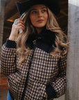 Woman in a black cowboy hat wearing the Wrangler Western houndstooth puffer jacket with black faux fur collar, leaning on a barn post